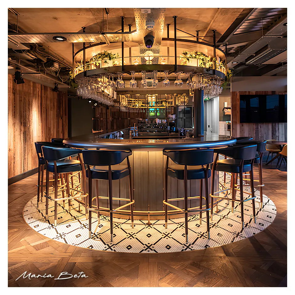 Barra de bar moderna con mobiliario de diseño, taburetes, iluminación decorativa y equipamiento profesional para hostelería.