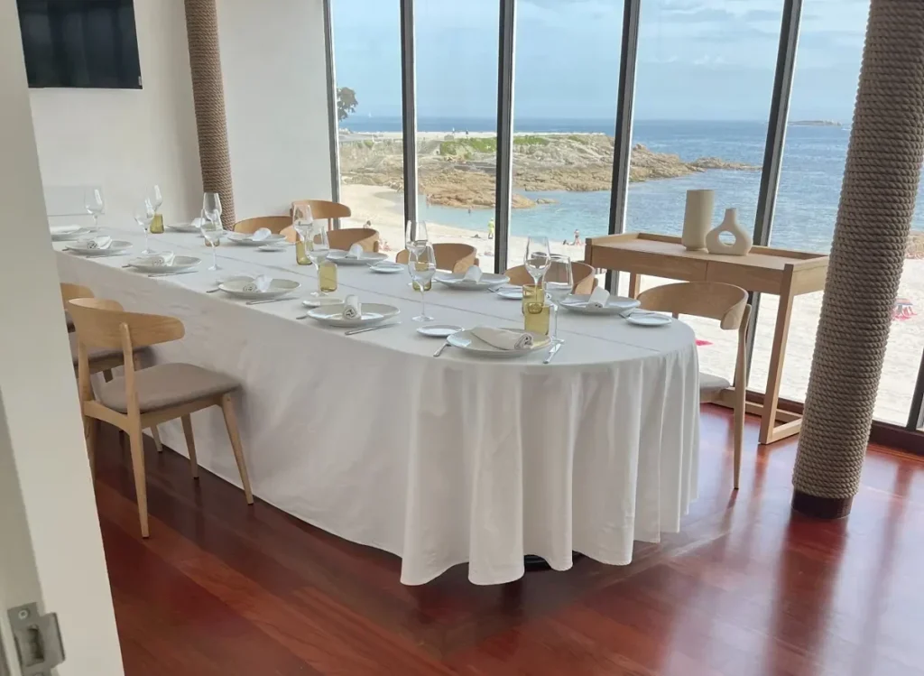 Mantelería blanca para mesa presidencial ovalada instalada por Currás y Salgado en el Restaurante Playa Club de A Coruña, con vistas al mar.